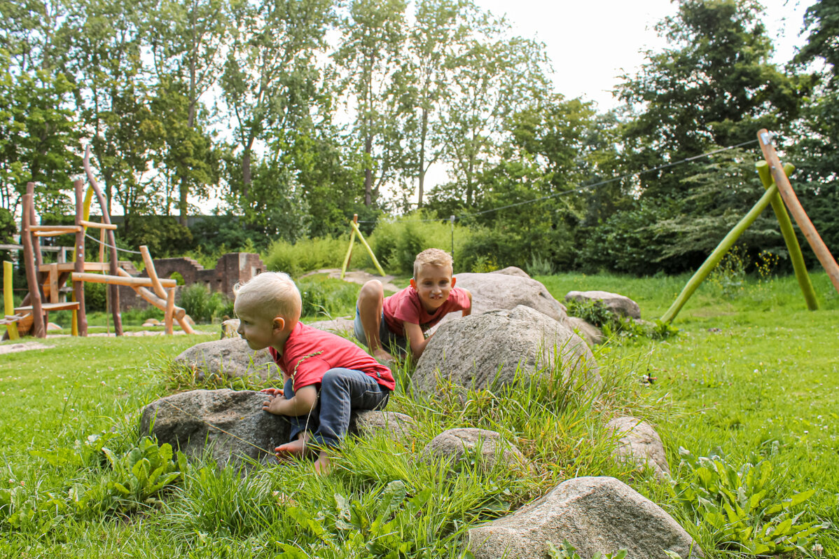 deux garçons jouent entre de grosses pierres dans la verdure devant une installation de jeux eibe