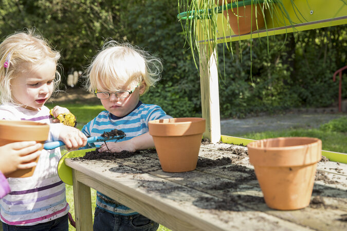 Kindergarten-Spielgeräte von eibe – zwei Kinder bepflanzen Blumentöpfe auf einer Holzbank.
